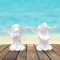 2 unpainted ceramic angel dogs standing on a wooden deck by the ocean.